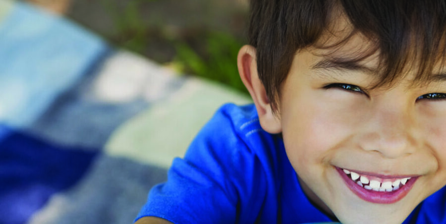 Smiling young boy in a blue shirt, close up, outdoors on a sunny day.
