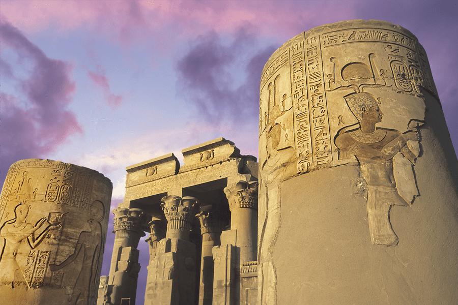 Ancient Egyptian temple ruins with carved columns at sunset, purple clouds in the sky.