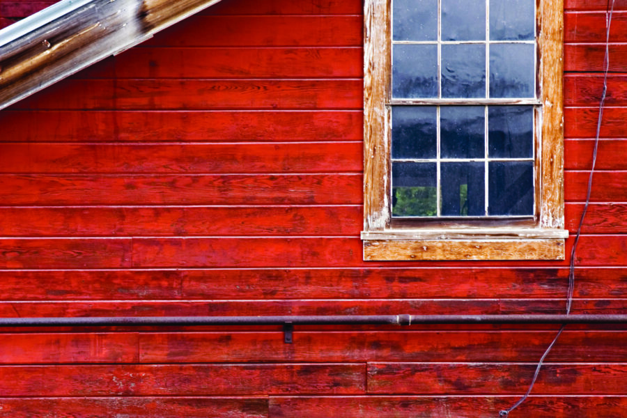 A weathered window on a red wooden wall with visible panels and a slanted roof edge above.