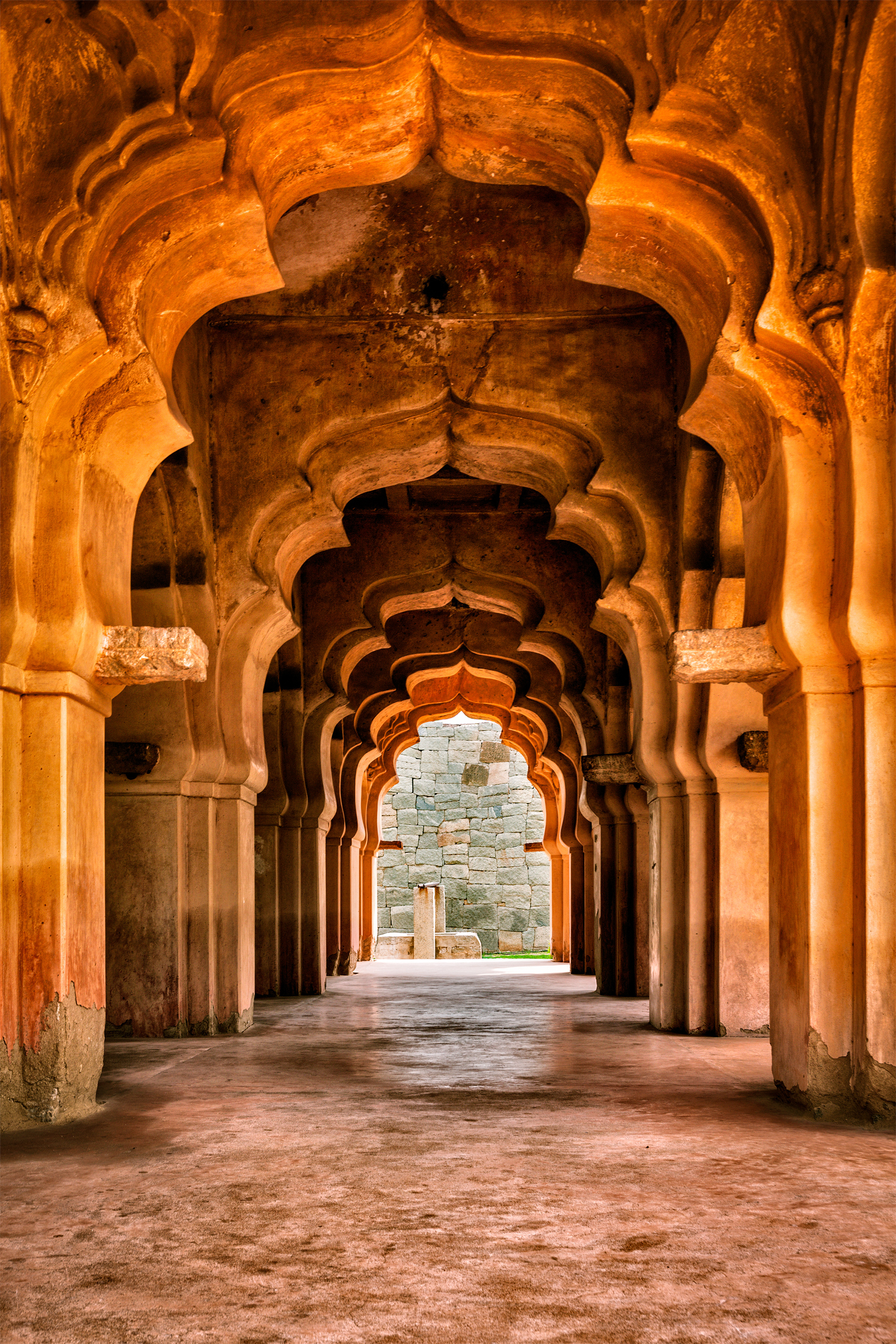 Arched hallway of an ancient palace, with sunlight highlighting detailed, ornate stone architecture.