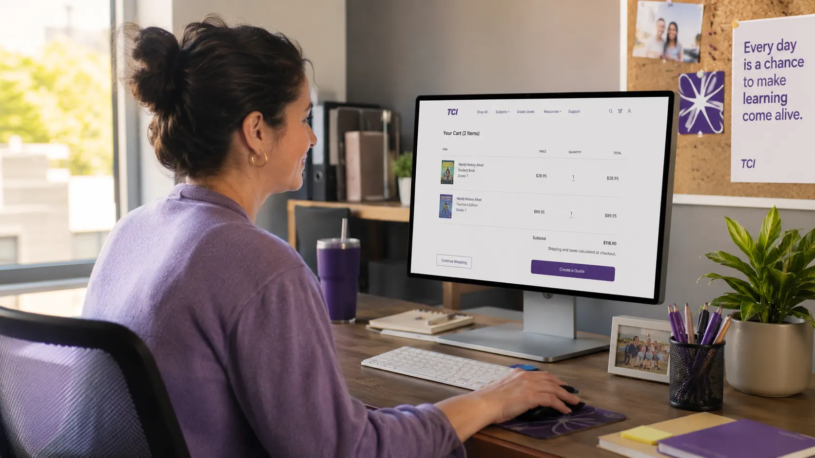 Woman in a purple sweater uses a desktop computer at a tidy office desk with a corkboard and plant nearby.