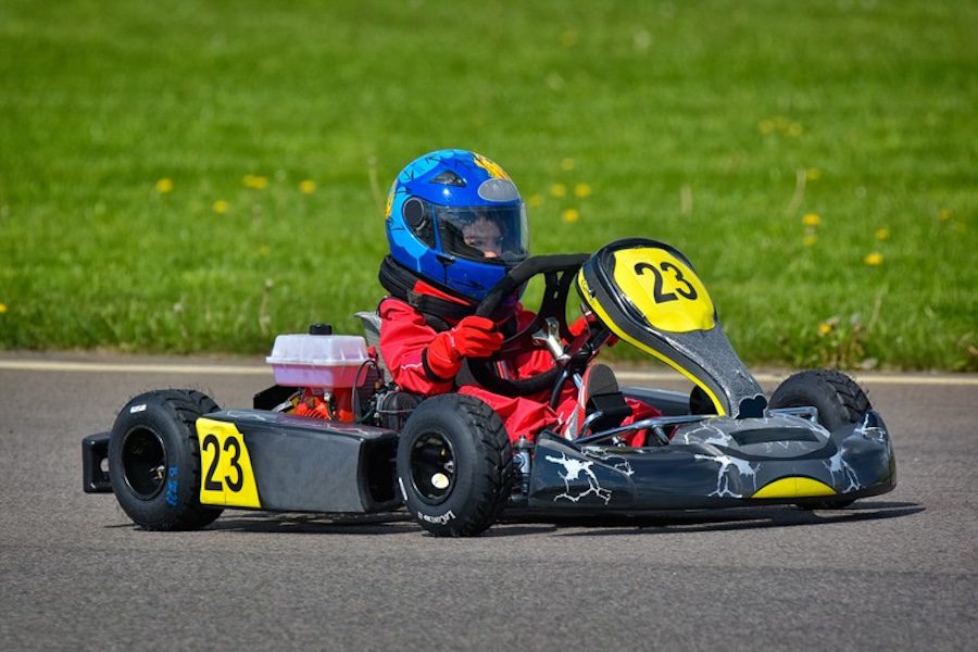 Child in a blue helmet and red suit driving a go-kart with number 23 on a racetrack.