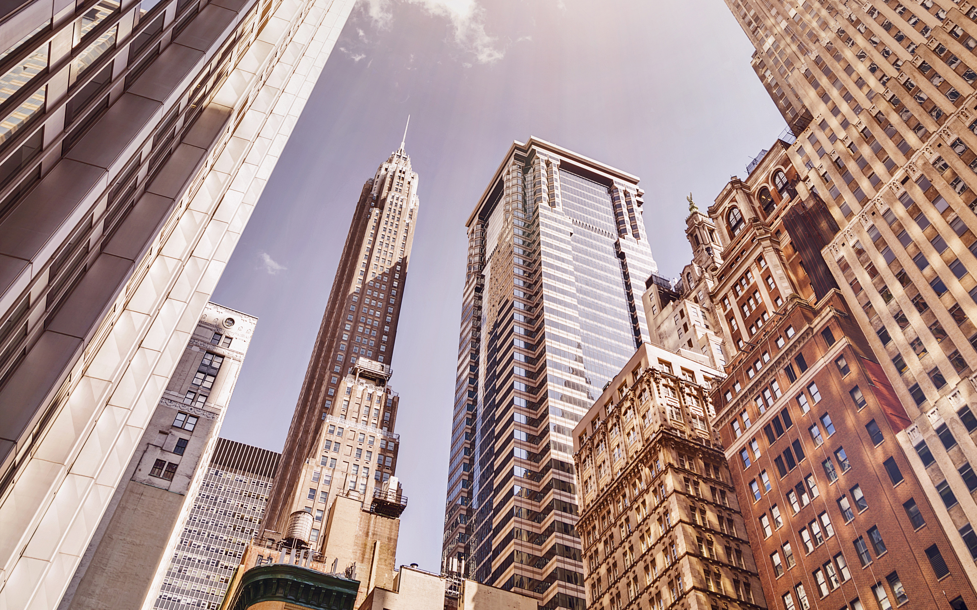 Tall skyscrapers in downtown city under a sunny sky, with sunlight streaming between the buildings.