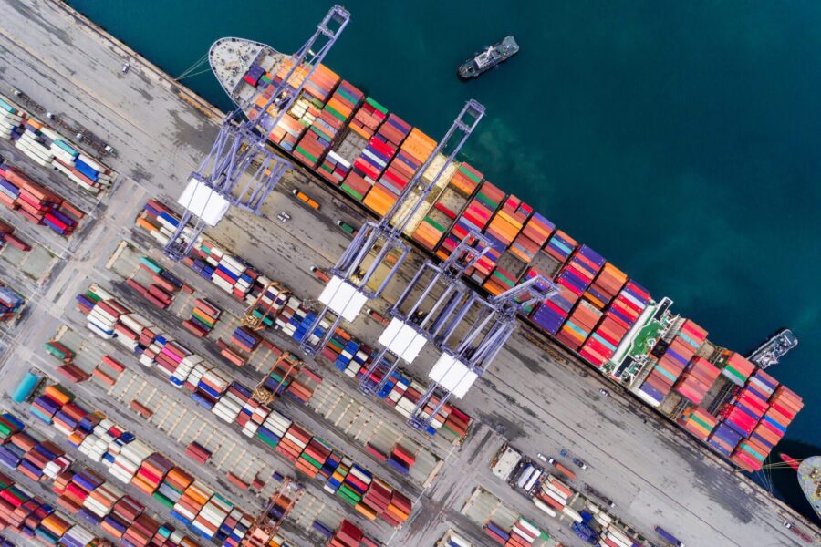 Aerial view of a cargo ship docked at a port with colorful shipping containers and cranes.