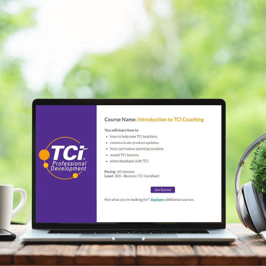 Laptop on desk displays Introduction to TCI Coaching course details, with coffee cup, plant, and headphones nearby.