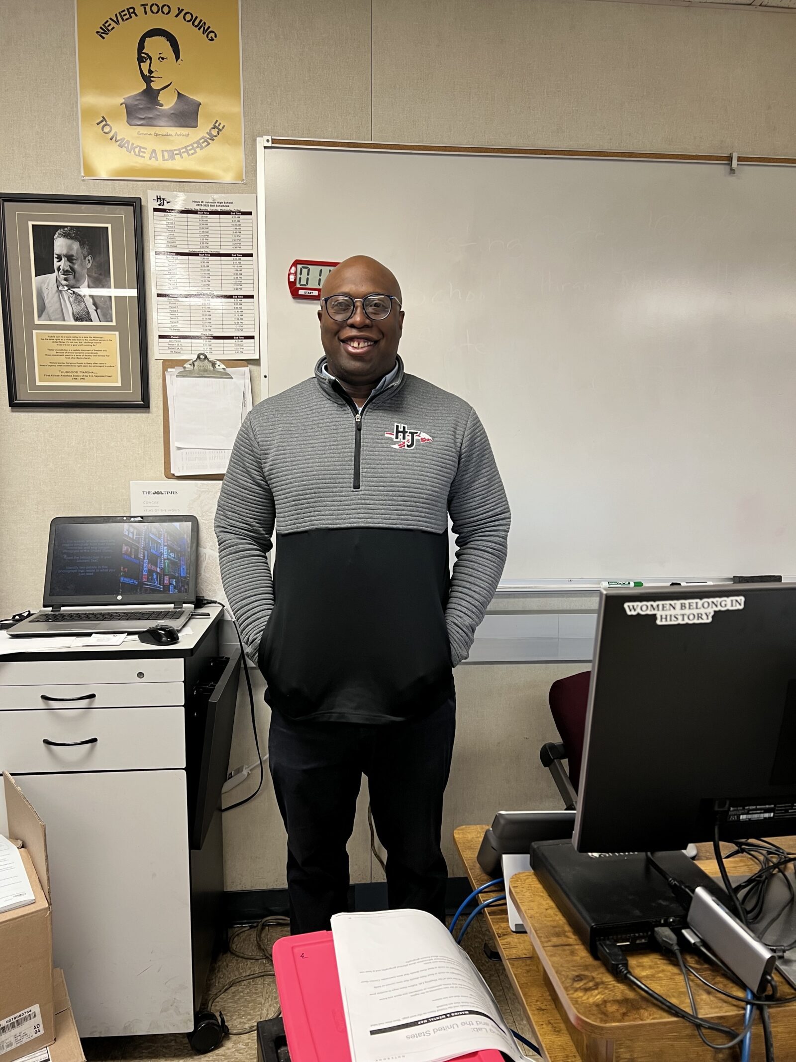 Teacher Michael Washington stands in front of a white board and next to a file cabinet and desk