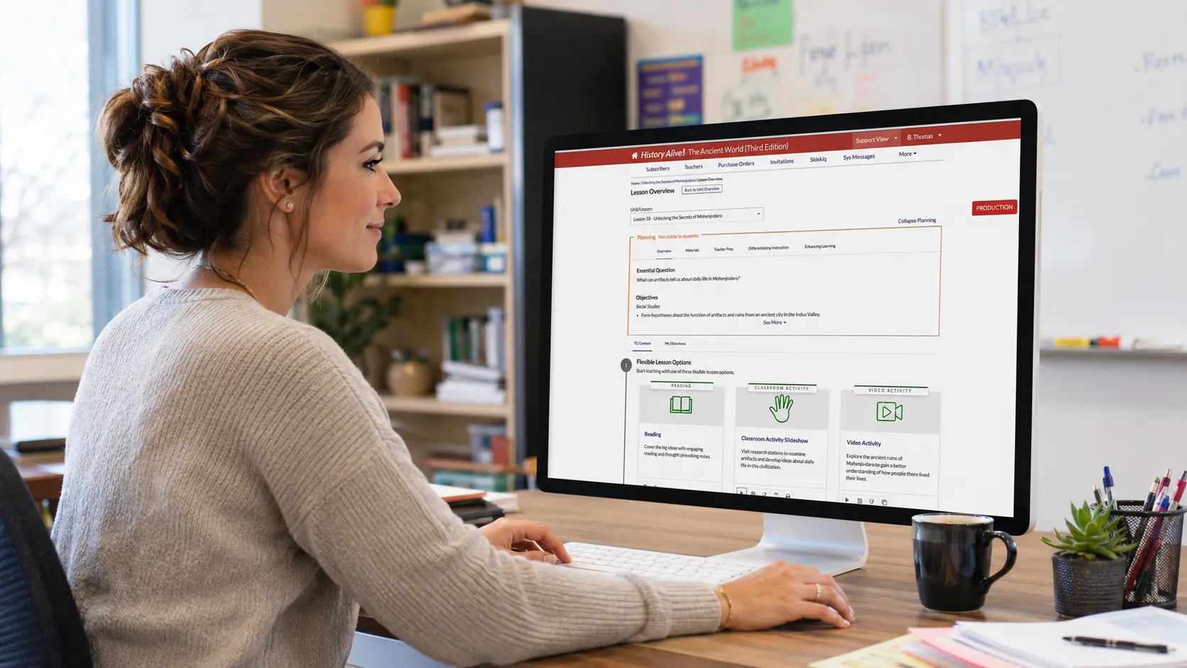 Woman sits at desk using a desktop computer in an office, viewing a website with educational resources on the screen.