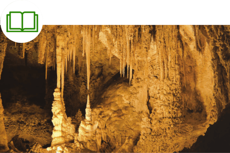 Stalactites and stalagmites inside a cave, illuminated with a warm yellow light.