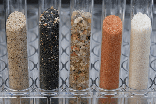 Five test tubes filled with different colored sand and gravel, arranged side by side in a holder.