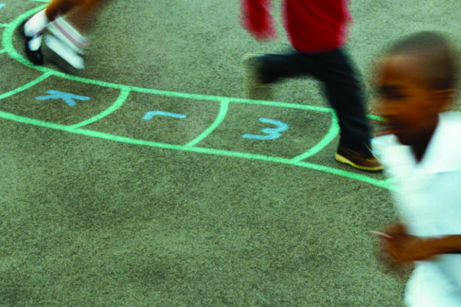 Children running on a playground, blurred in motion, with chalk numbers drawn on the ground.