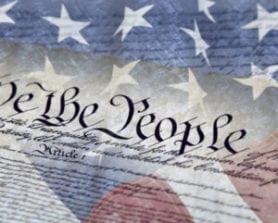 Close-up of the U.S. Constitutions We the People text overlaid with part of the American flag.