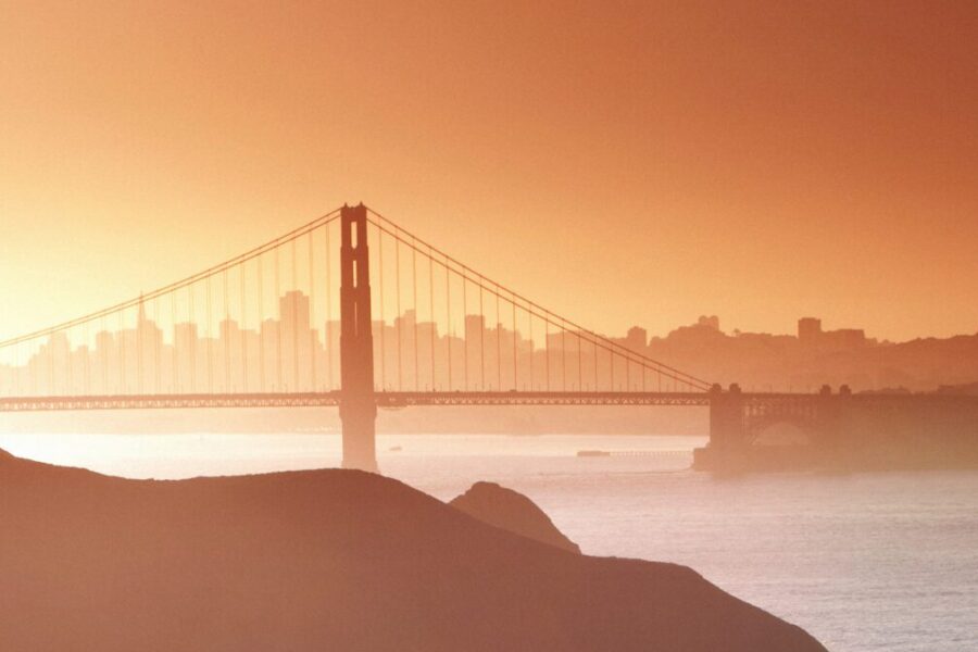 Golden Gate Bridge at sunset with a hazy city skyline and water in the background.
