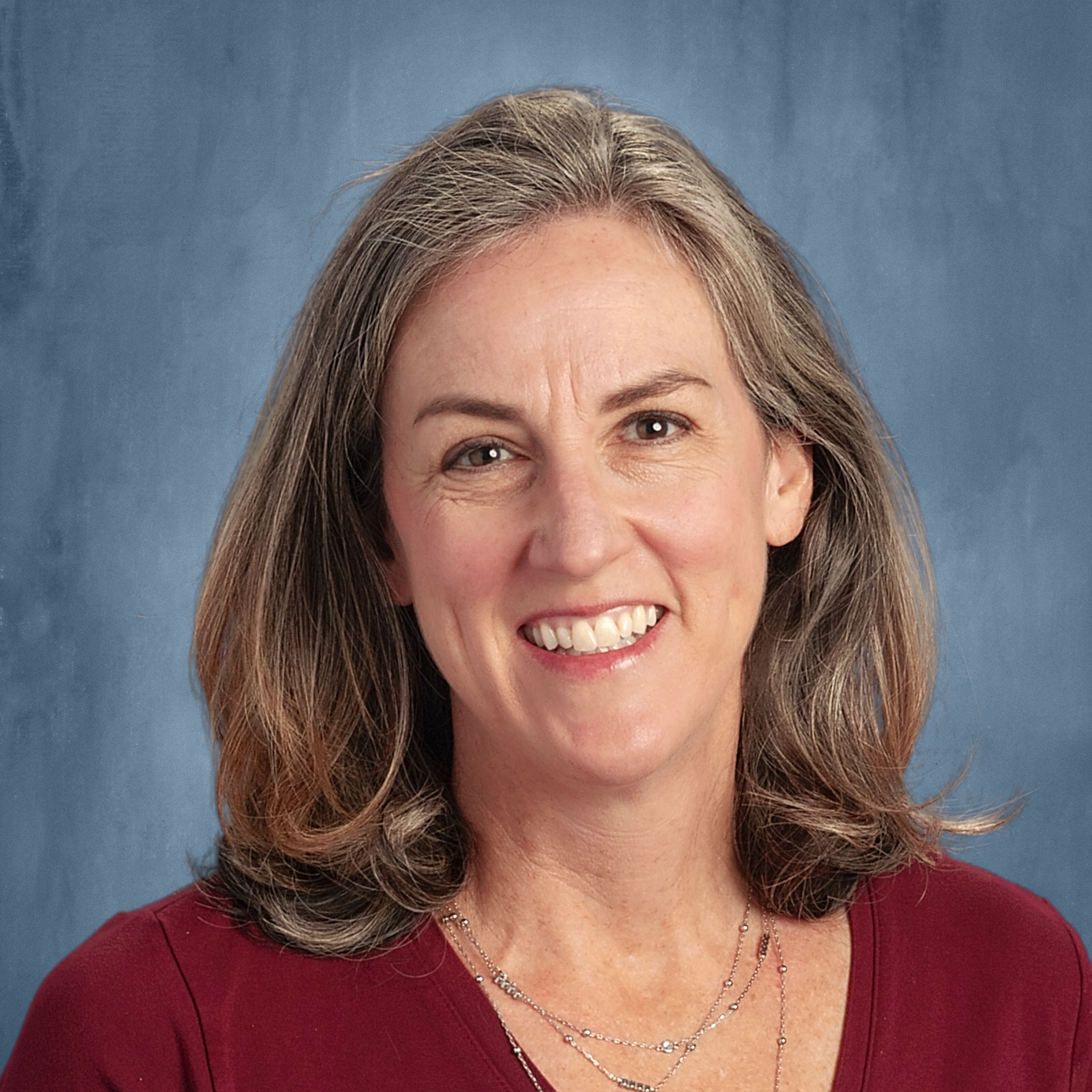 Smiling woman with shoulder-length brown hair wearing a burgundy top, against a blue background.