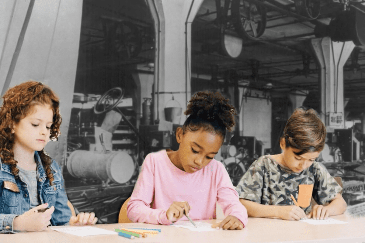 Three children sit at a desk drawing, with a black and white factory background behind them.
