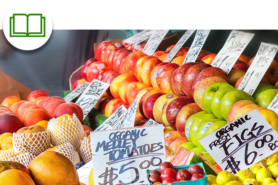 Various fresh fruits, including apples and peaches, are displayed for sale with handwritten price signs at a market.