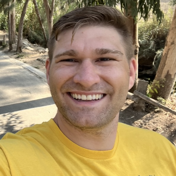 Andrew Esposito outdoors on a sunny day, trees and a path visible in the background.
