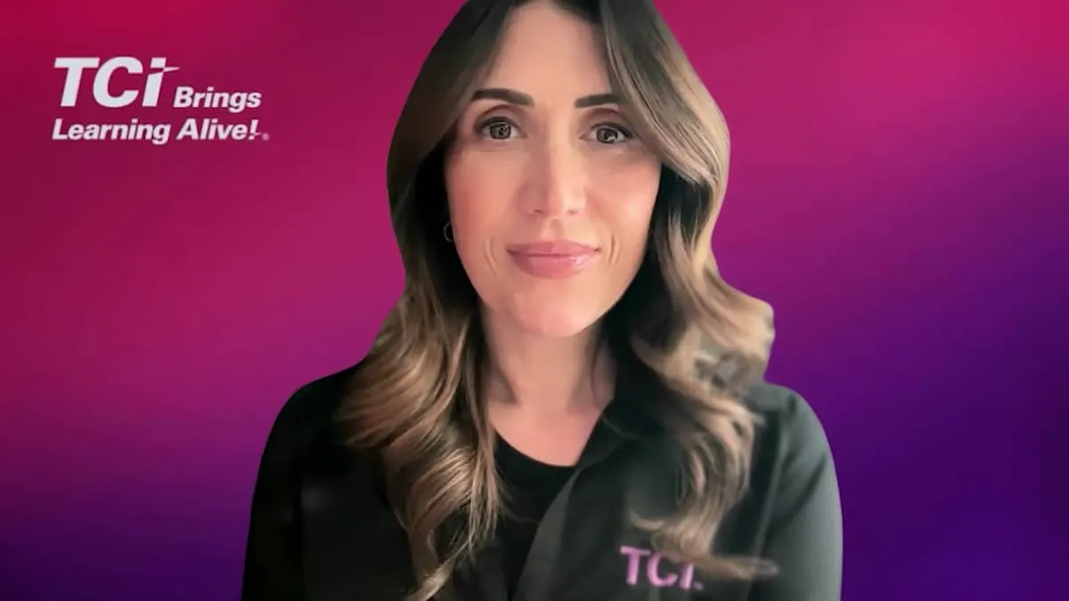 Woman with wavy brown hair in a black TCI shirt, smiling in front of a pink and purple background with TCI logo.
