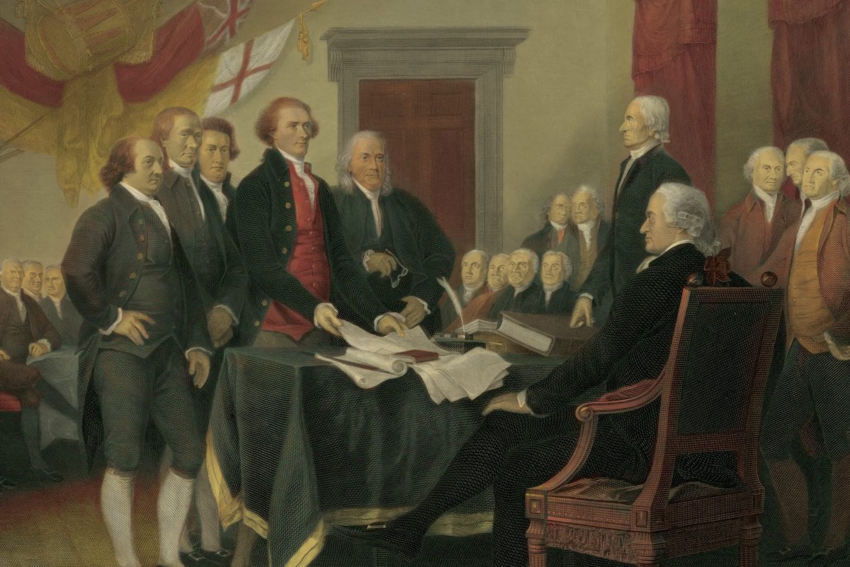 Men in 18th-century clothing sign the Declaration of Independence in a formal room with flags and documents.