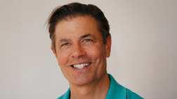 A smiling man wearing a bright teal polo shirt.