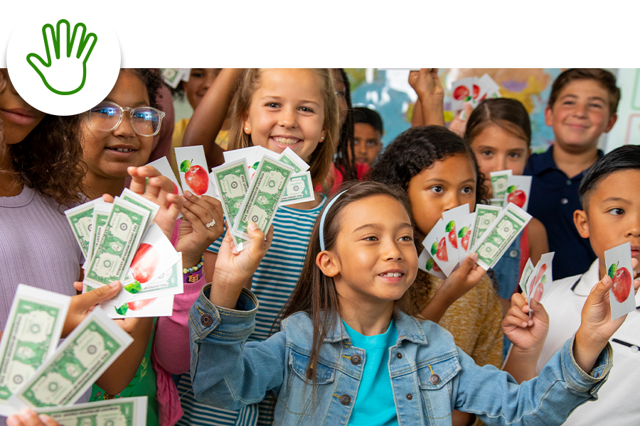 Children smiling and holding play money and cards with apples in a classroom setting.