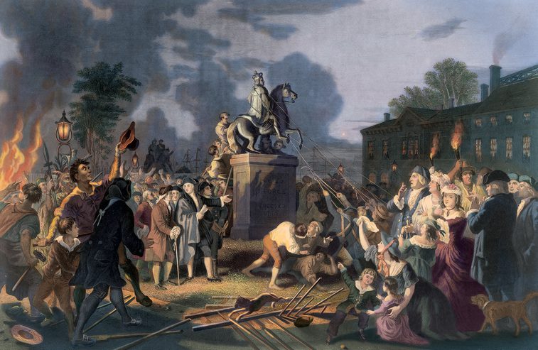Crowd pulls down a statue of a man on horseback while buildings burn in the background during a night revolt.