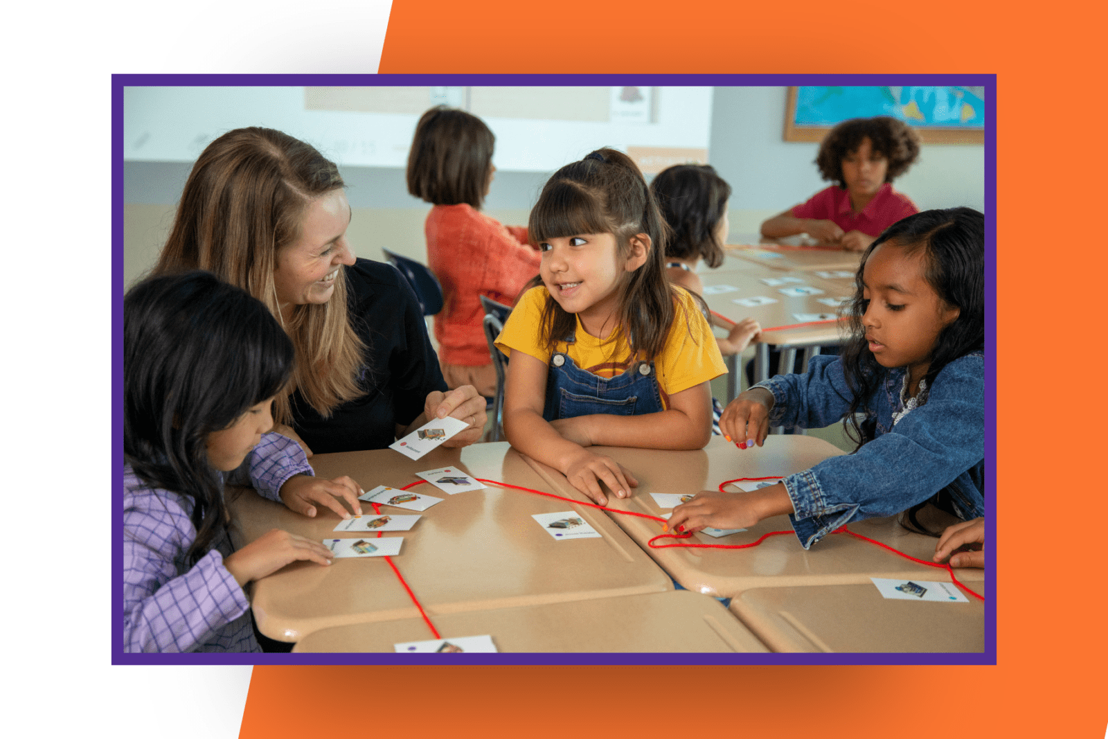 A teacher and three students sit at desks, connecting small picture cards with a red string.