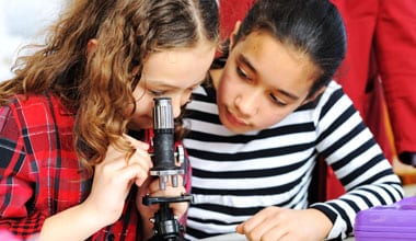 Two girls looking through a microscope in a classroom.