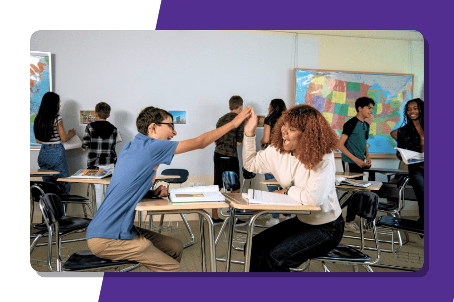 Two students high-five while sitting at desks in a classroom.