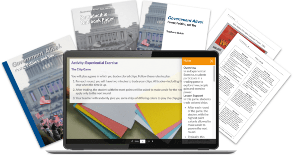 A laptop displays a lesson with books, notebook pages, and worksheets about government arranged behind it.