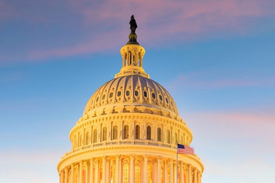 The U.S. Capitol dome at sunset, illuminated with a clear sky and an American flag visible to the right.