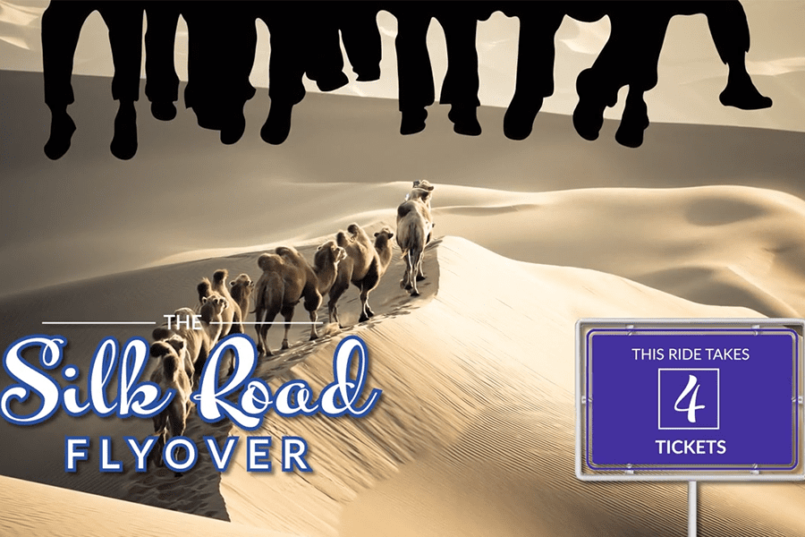 A camel caravan walks in sand dunes; silhouettes of feet dangle above; sign says ride takes 4 tickets.