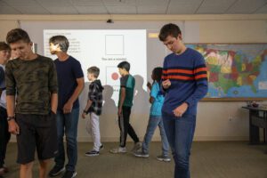 Students play the dot game. One student looks at his paper slip to see if he has a dot.